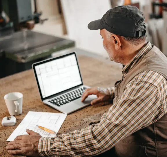 Man working on laptop with blueprints.